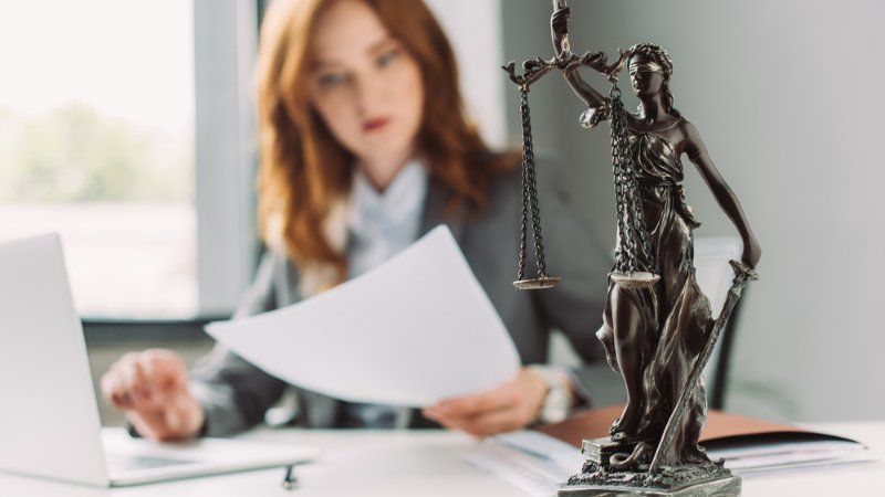 A woman is sitting at a desk with a statue of justice.