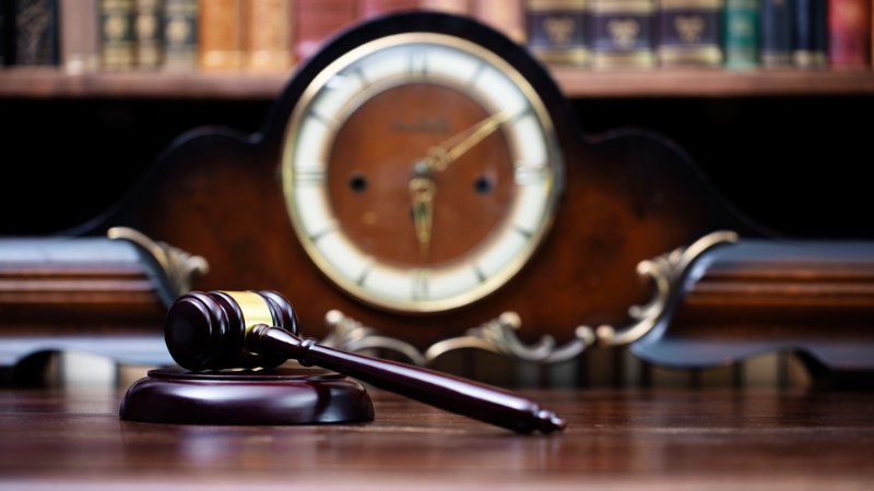 A judge 's gavel is sitting on a wooden table in front of a clock.