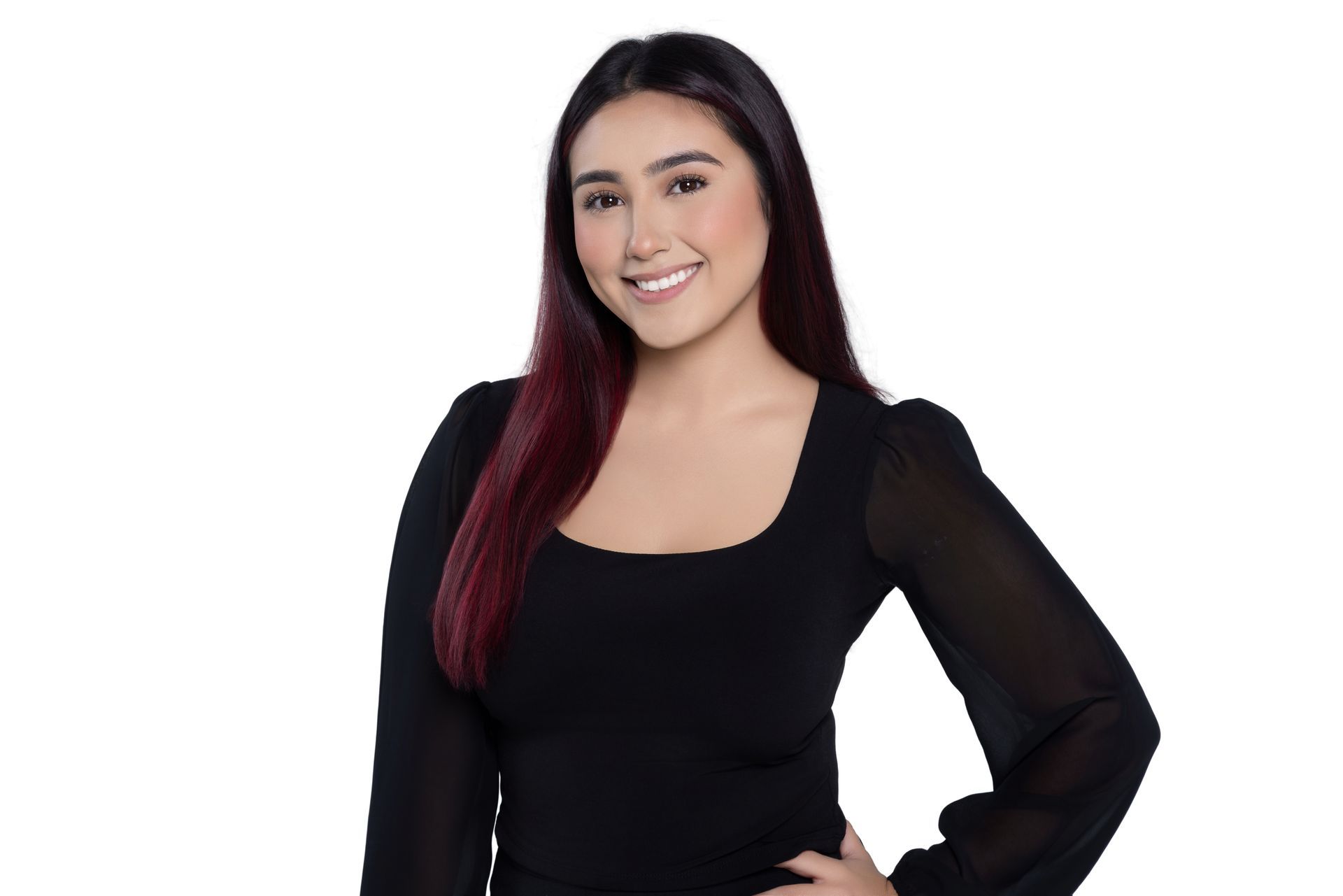 A person with long, dark hair with reddish highlights smiling, wearing a black long-sleeved top against a white background.