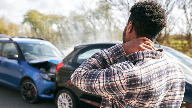 A man is holding his neck in pain in front of a car accident.