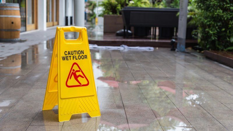 A yellow caution wet floor sign is sitting on a wet tiled floor.