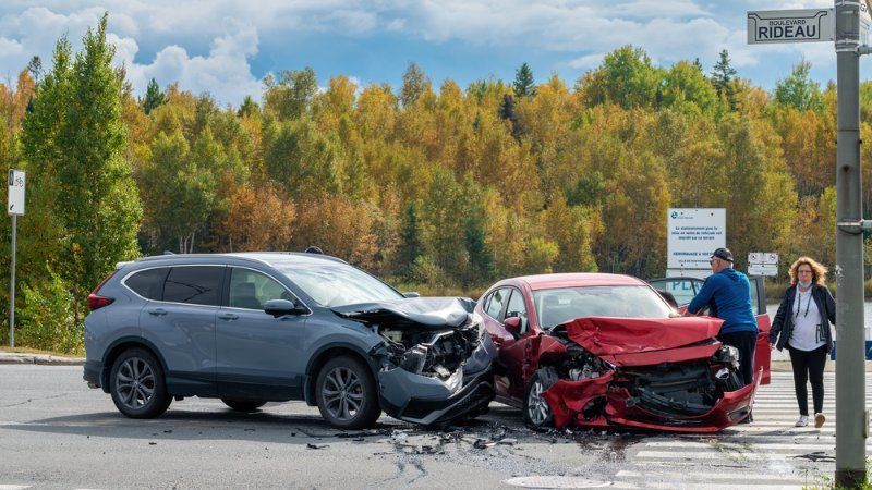 A gray SUV and a red sedan are involved in a collision at an intersection with people standing nearby.