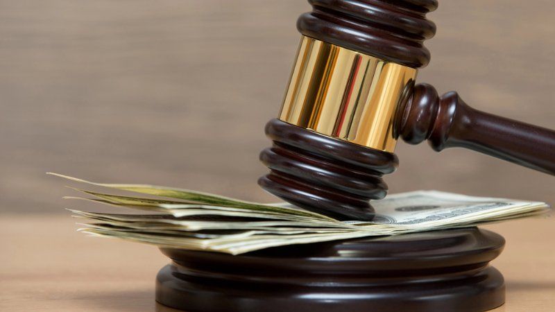 A wooden judge's gavel resting on a stack of US dollar bills on a desk.