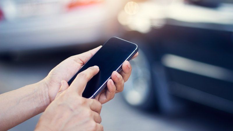 A person is using a cell phone in front of a car.