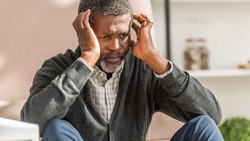 A man is sitting on the floor with his hands on his head.