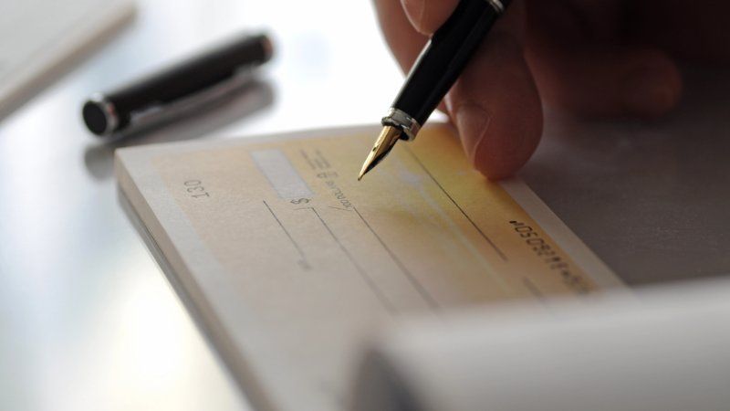 A person holding a fountain pen, poised to write on a blank personal check.