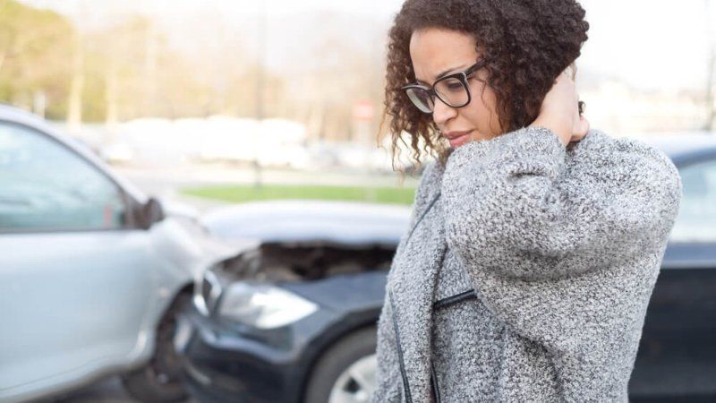 A woman is standing in front of a car that has been involved in a car accident.