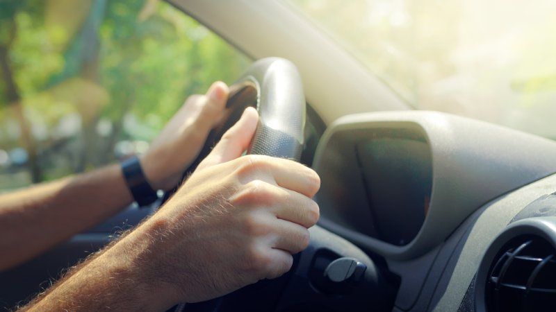 A person is driving a car with their hands on the steering wheel.