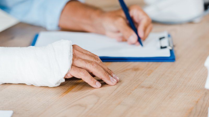 A person with a cast on their arm is writing on a clipboard.