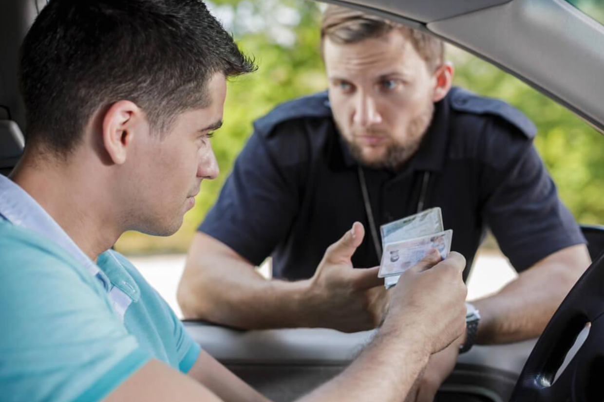 A man is sitting in a car talking to a police officer, wondering,