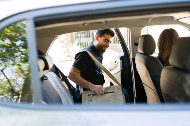 A man is loading his bag into the back seat of a car.