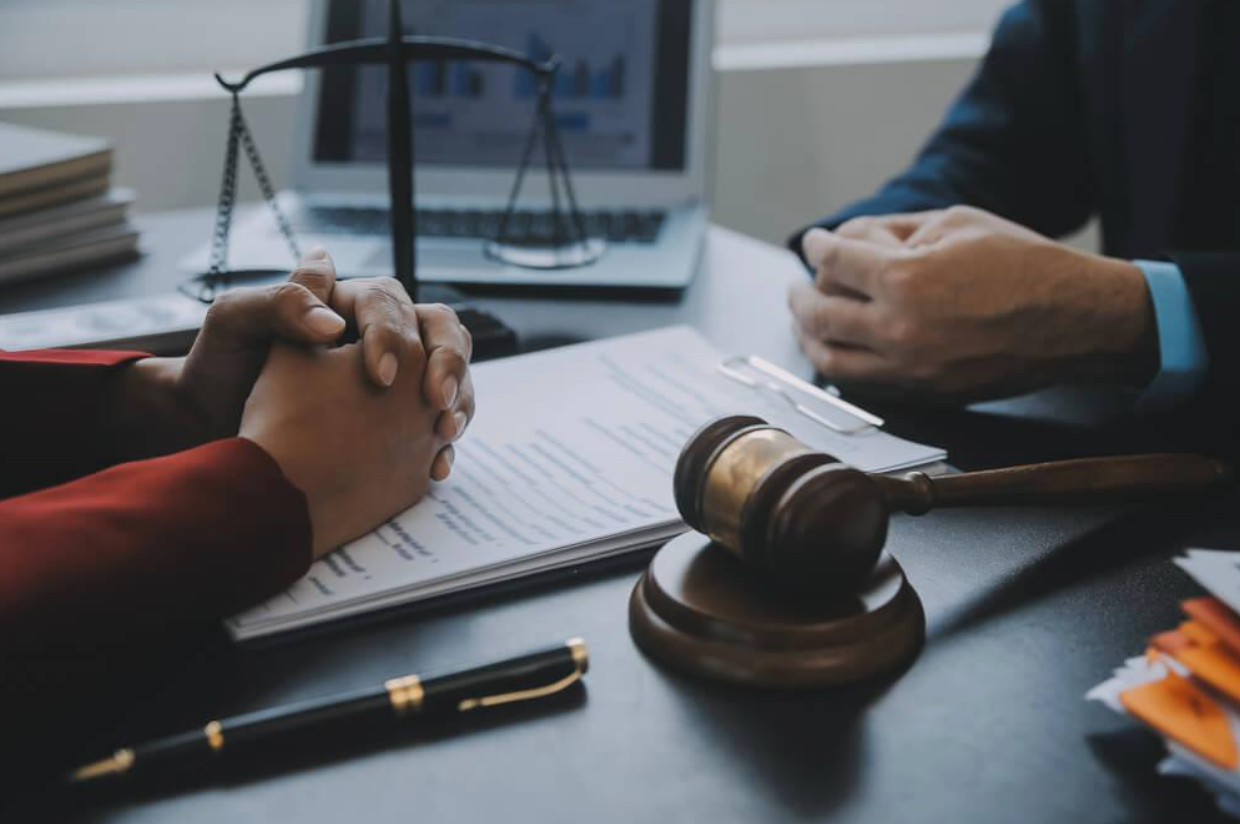 Two people are sitting at a table with a judge 's gavel and scales of justice.