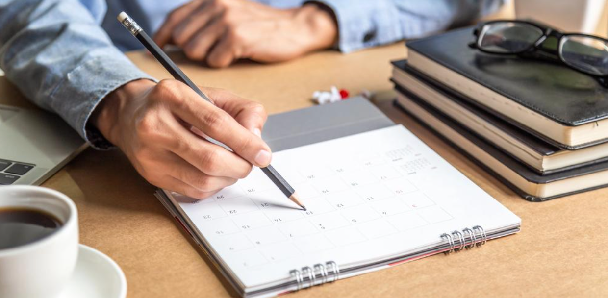 A person is writing on a calendar with a pencil.