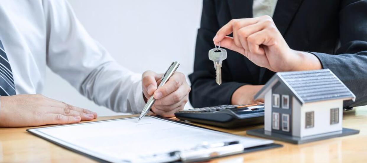 A man is holding a key while a woman signs a document.