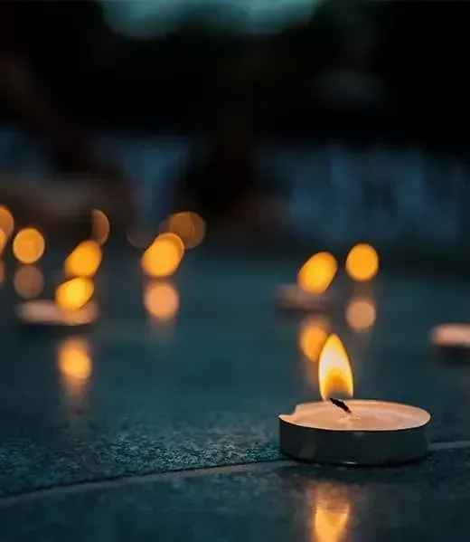 Small tea light candles glow softly on a dark, reflective surface in a tranquil, dimly lit setting.