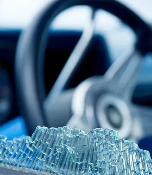 Shattered tempered glass fragments in the foreground with a blurred car steering wheel in the background.