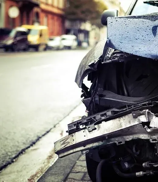 A close-up view of a blue car with significant front-end damage, parked on a city street.