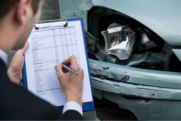 A man is writing on a clipboard in front of a damaged car.