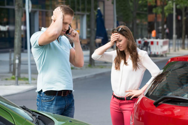 A man is talking on a cell phone while a woman stands next to a green car.