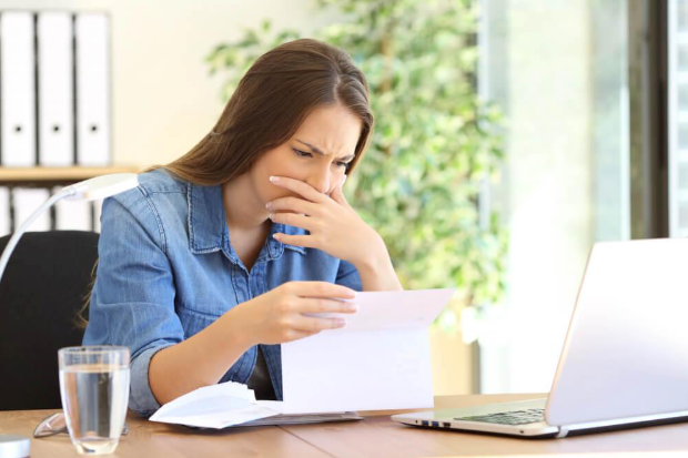A woman is sitting at a desk looking at a piece of paper.