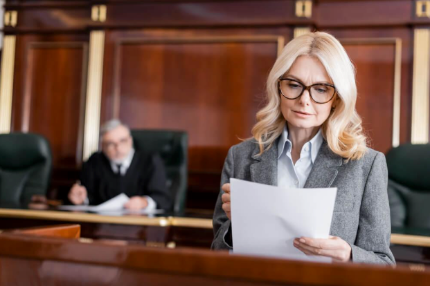 A woman is holding a piece of paper in front of a judge in a courtroom.