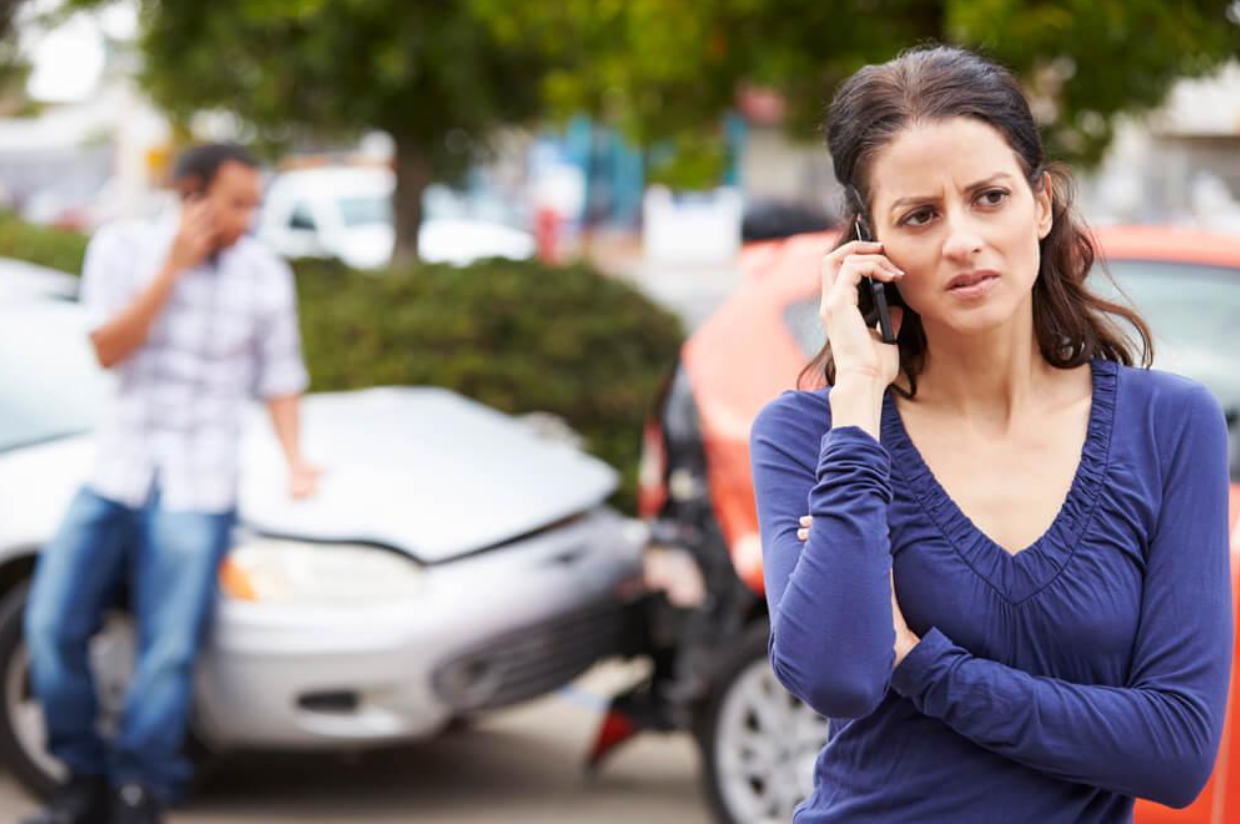 A woman is talking on a cell phone in front of a car accident.