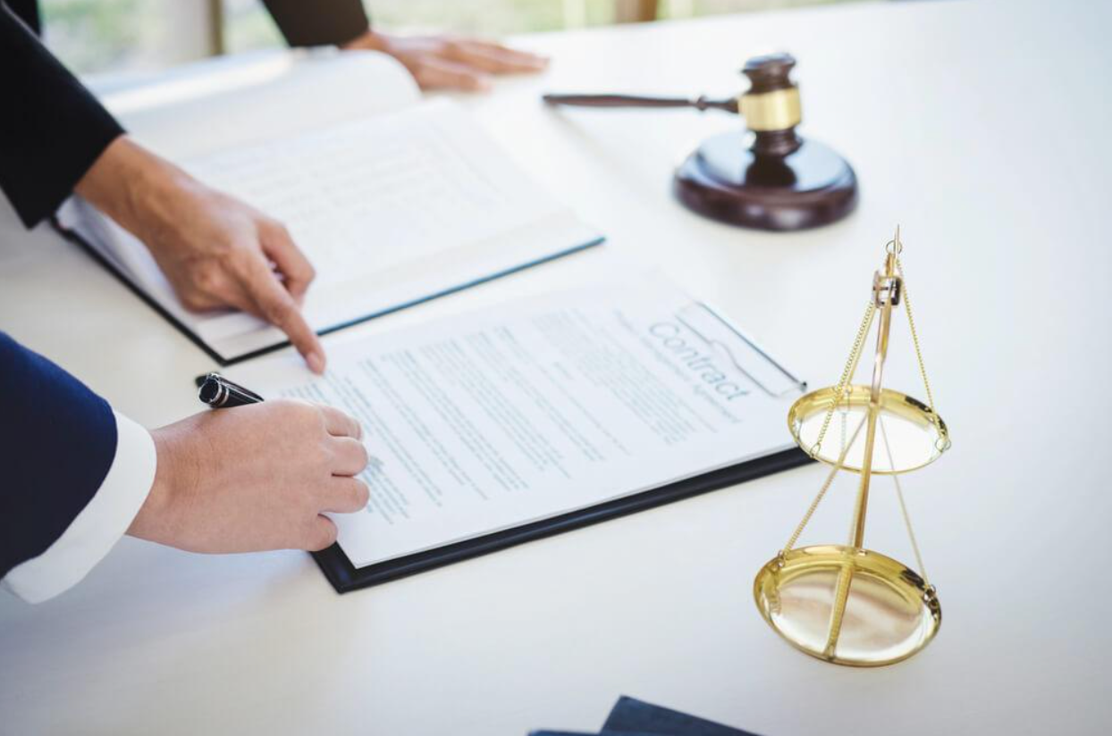 A person is signing a document next to a scale of justice.