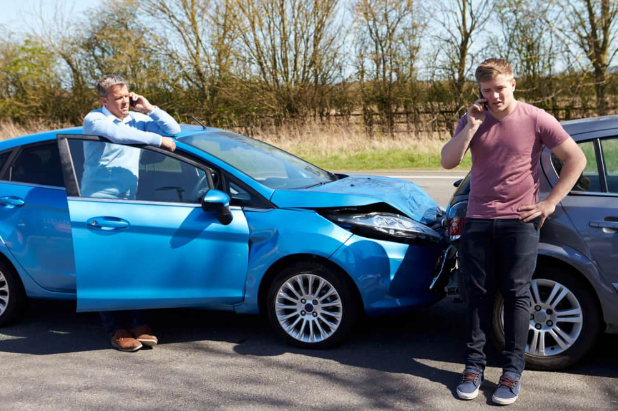 Two men are standing next to a blue car that has been damaged in a car accident.