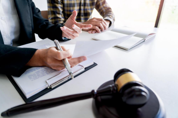 A couple of people are sitting at a table with papers and a judge 's gavel.