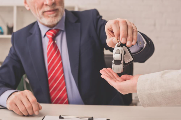 A man in a suit and tie is giving a car key to a woman.
