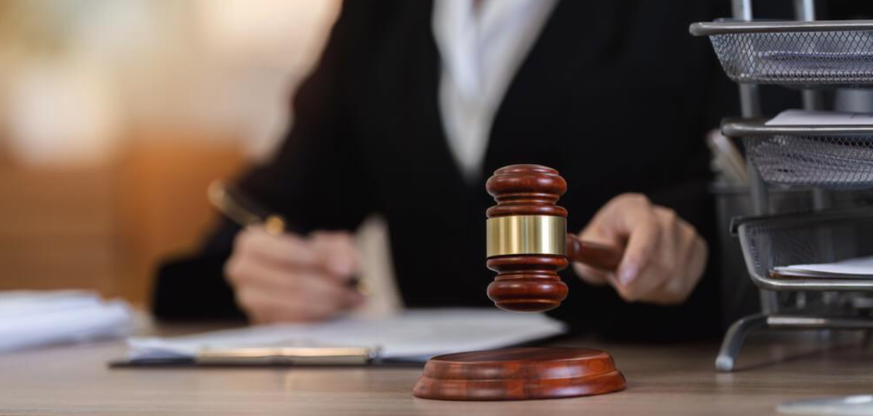 A judge is sitting at a desk holding a wooden gavel.