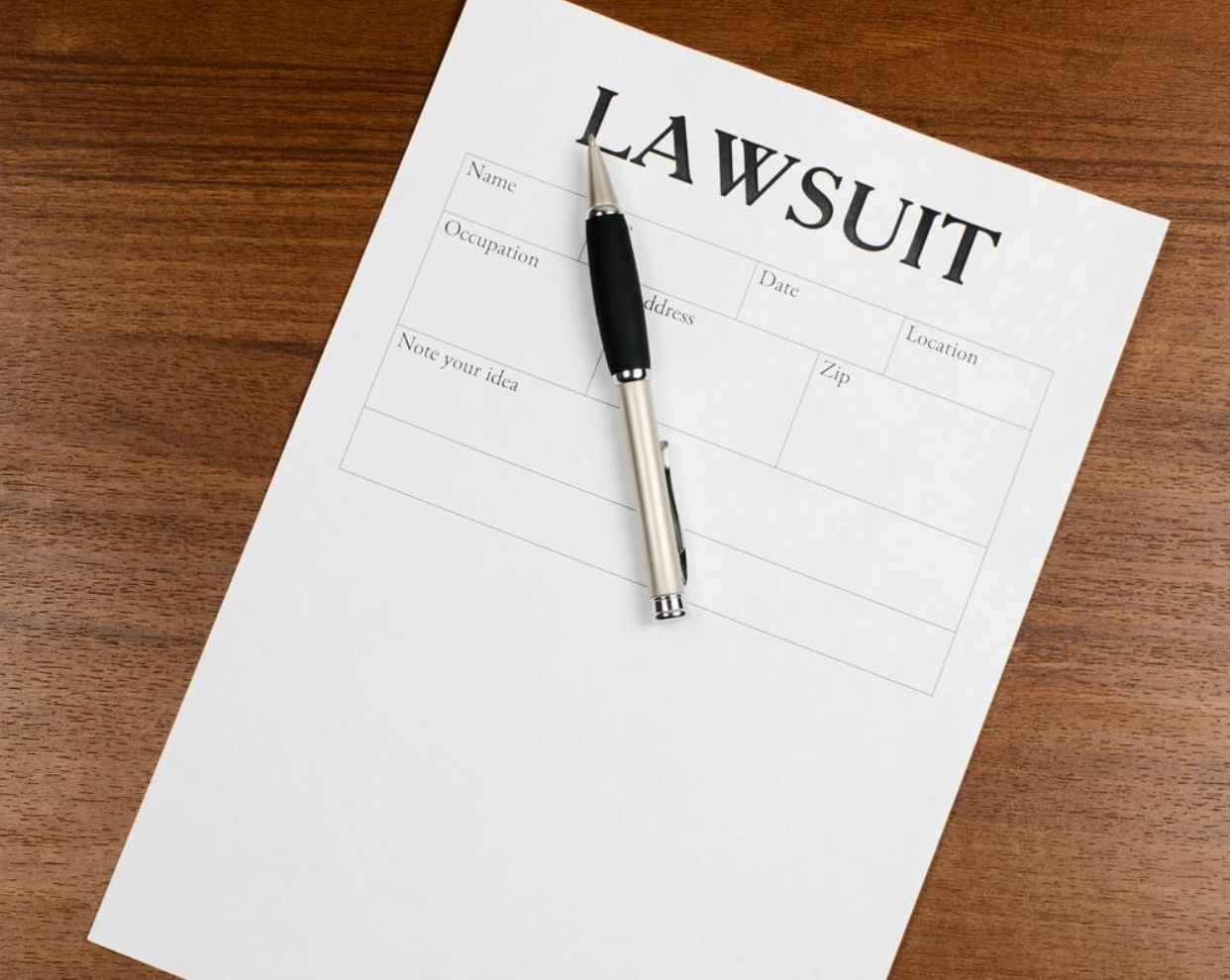 A pen is sitting on top of a lawsuit form on a wooden table.