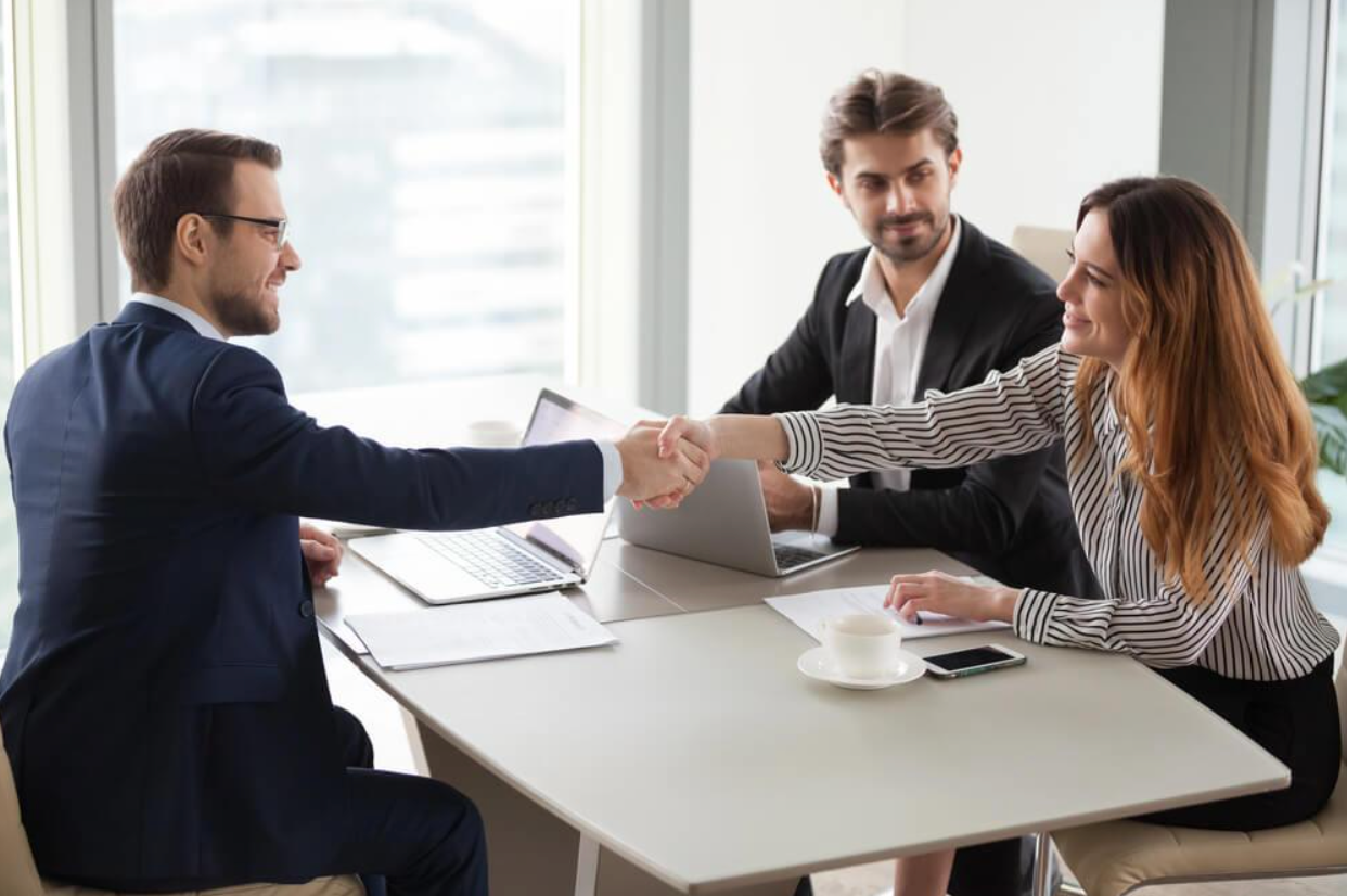 A man and a woman are shaking hands while sitting at a table.