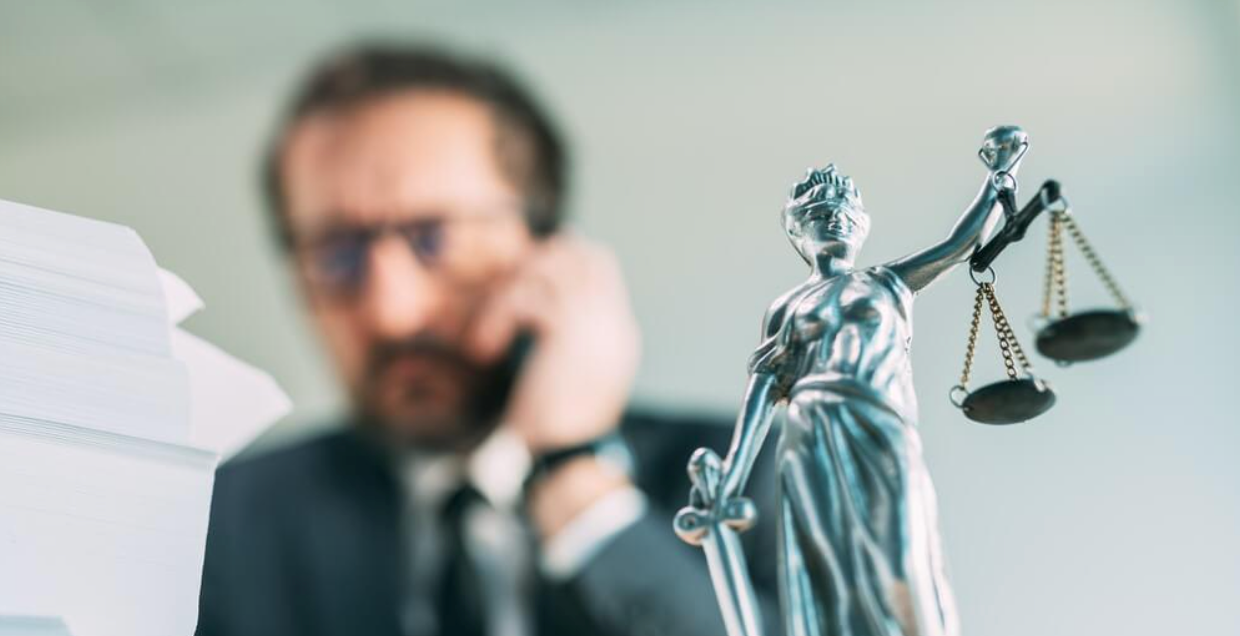 A man is talking on a cell phone next to a statue of justice.