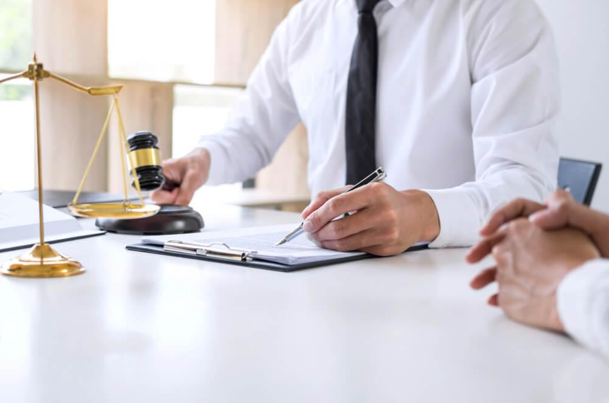 A man is sitting at a table holding a gavel and writing on a clipboard.