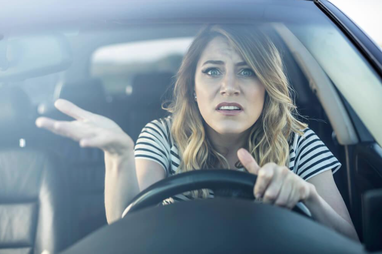 A woman is driving a car and making a funny face.