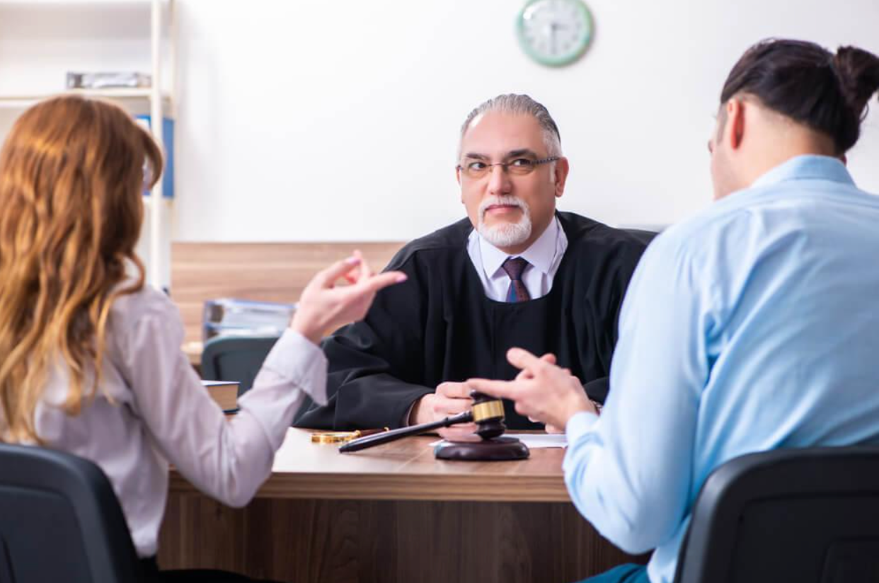 A man and a woman are sitting at a table talking to a judge.