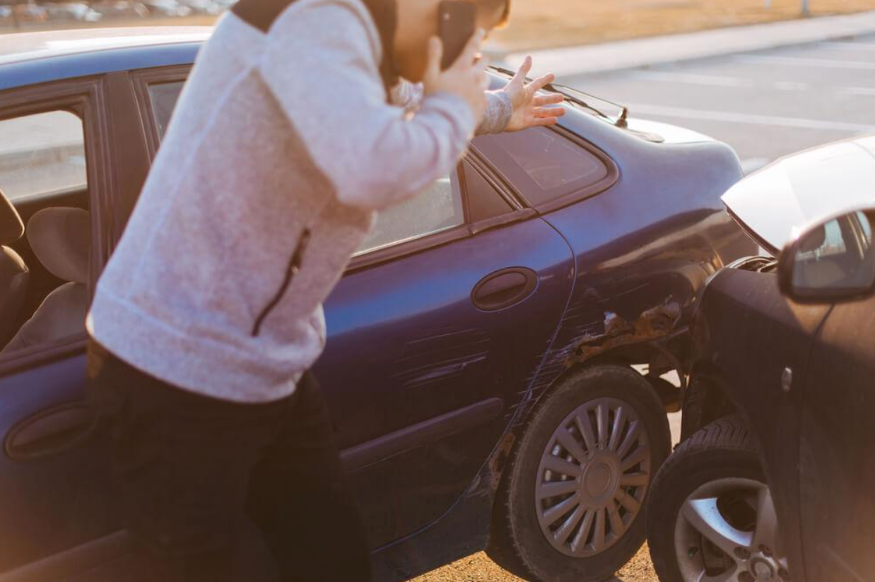 A man is talking on a cell phone next to a car that has been involved in a car accident.
