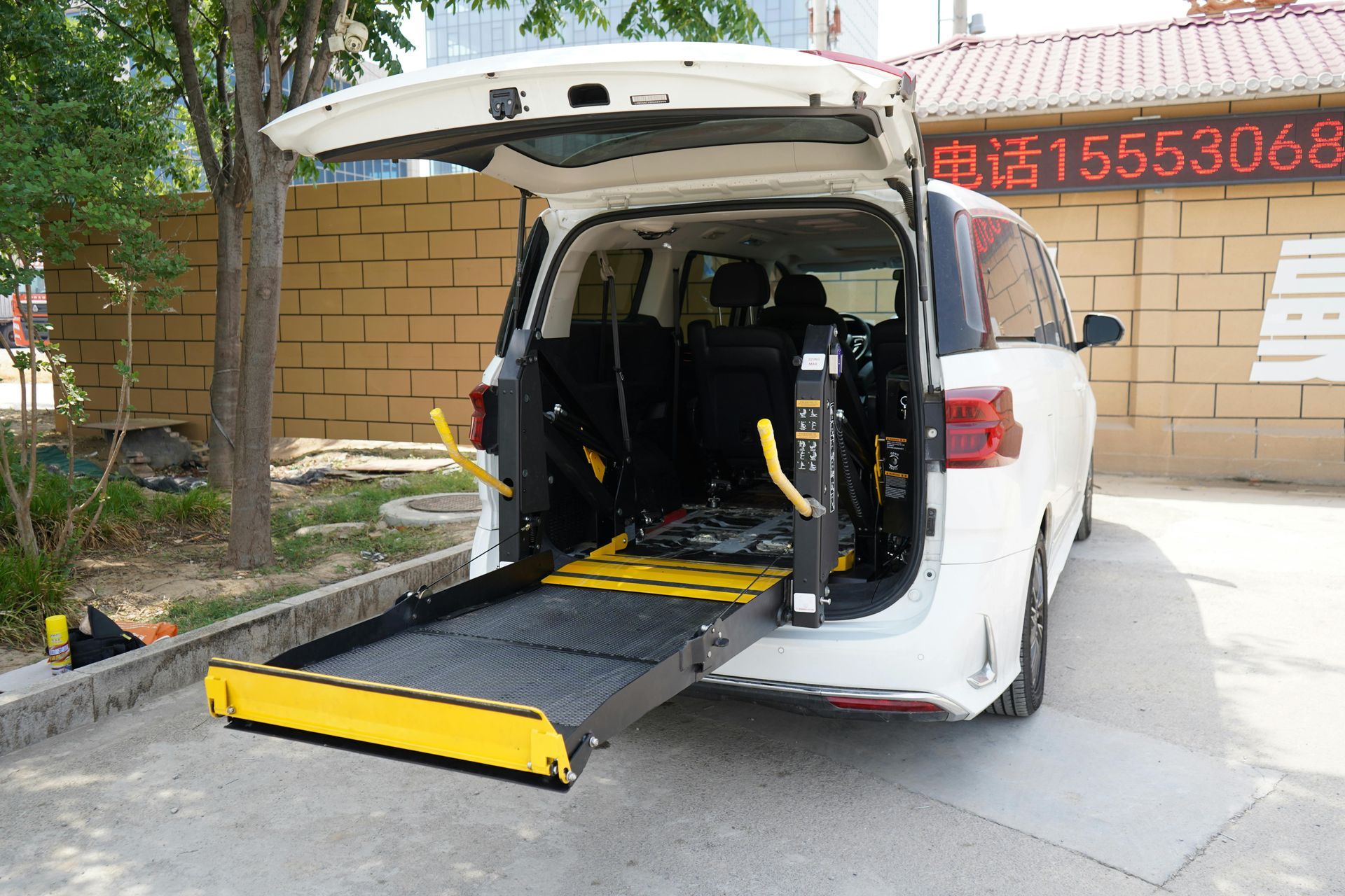 A white van with its rear door open and an extended yellow and black wheelchair lift ramp deployed on the ground.