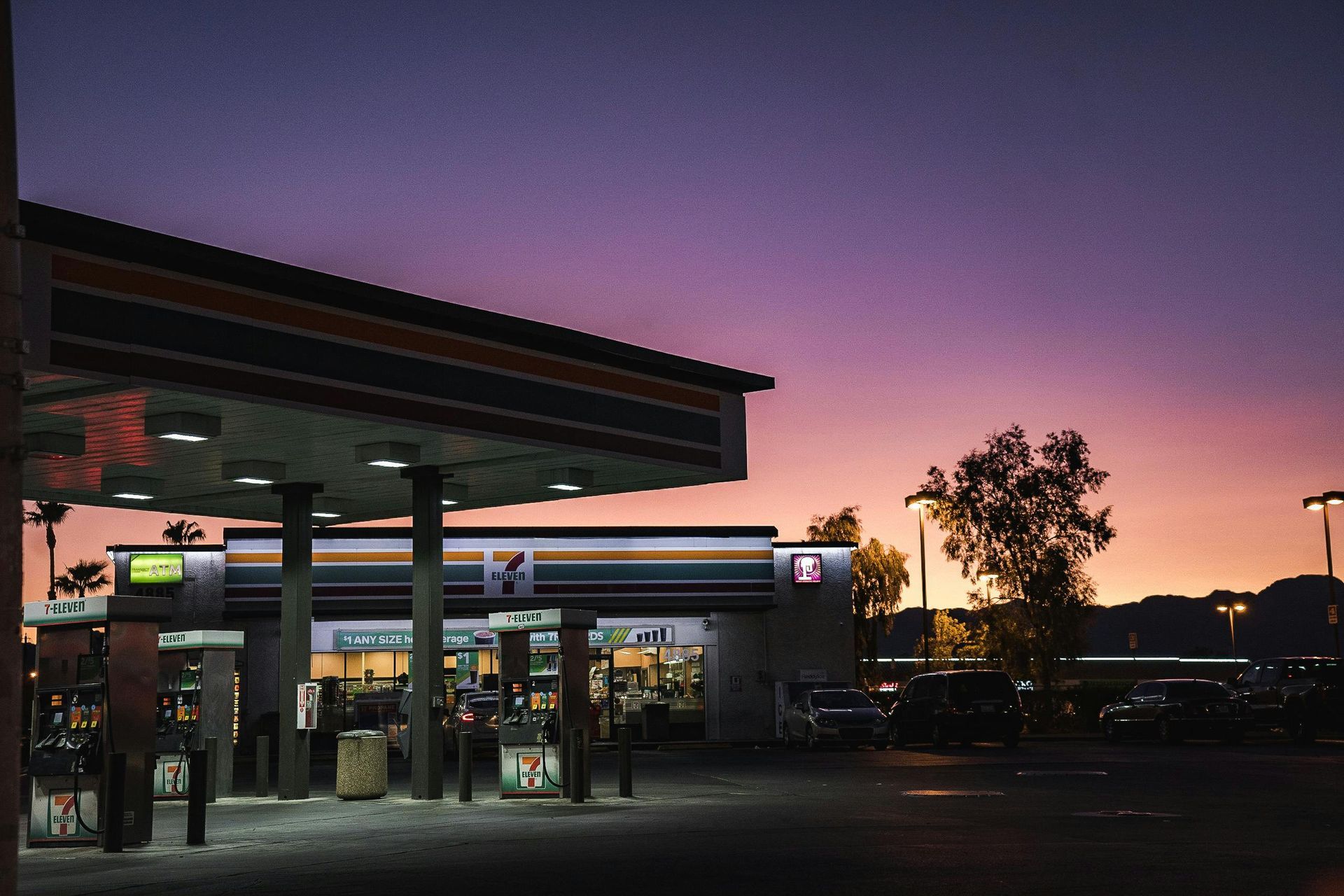 A 7-Eleven gas station under a vibrant purple and orange sunset sky.