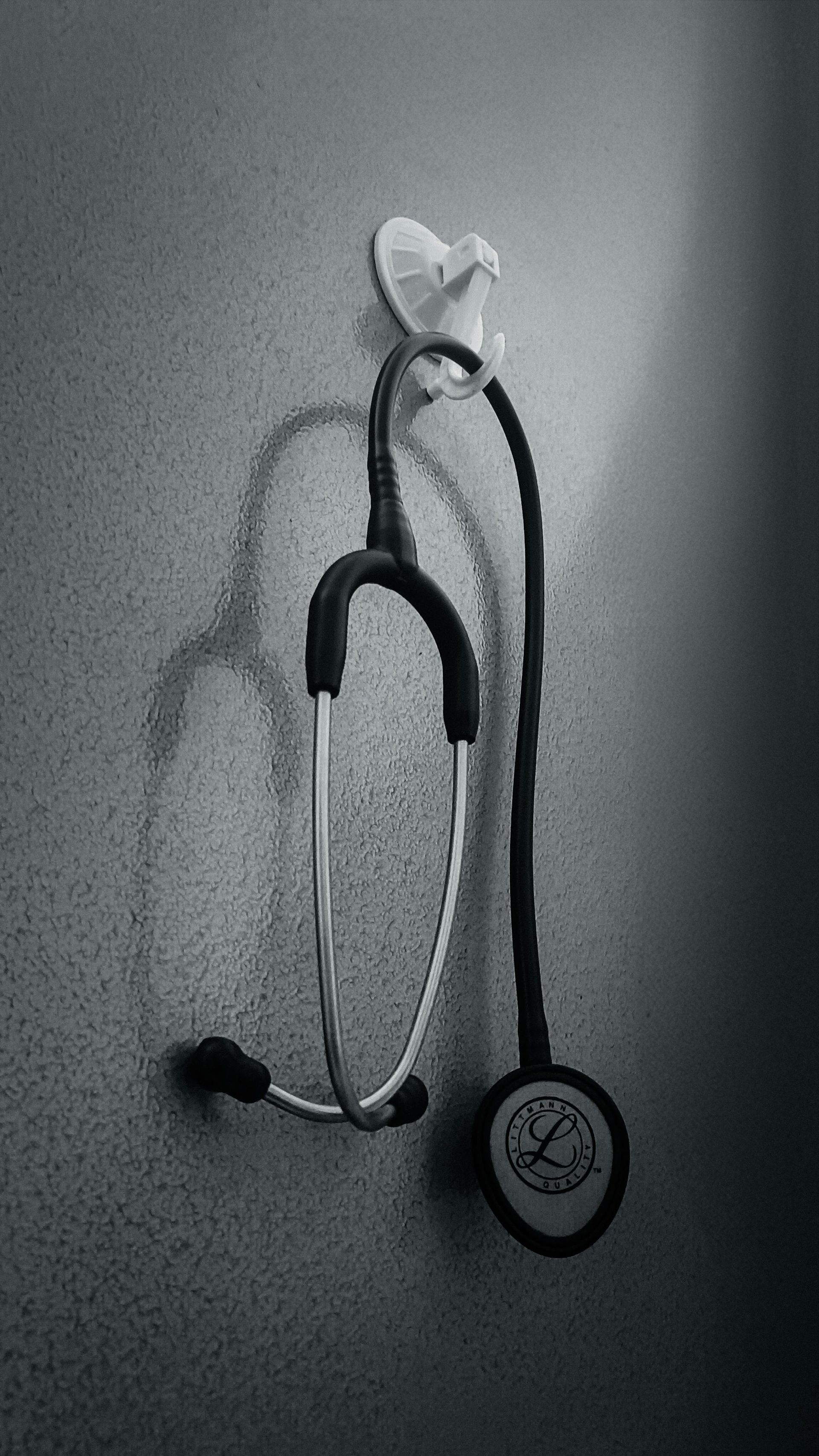 A black stethoscope hangs on a small wall-mounted hook against a textured gray background.