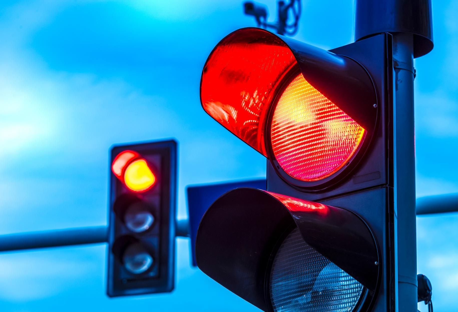 Two traffic lights against a blue sky, both showing a red light to stop traffic.
