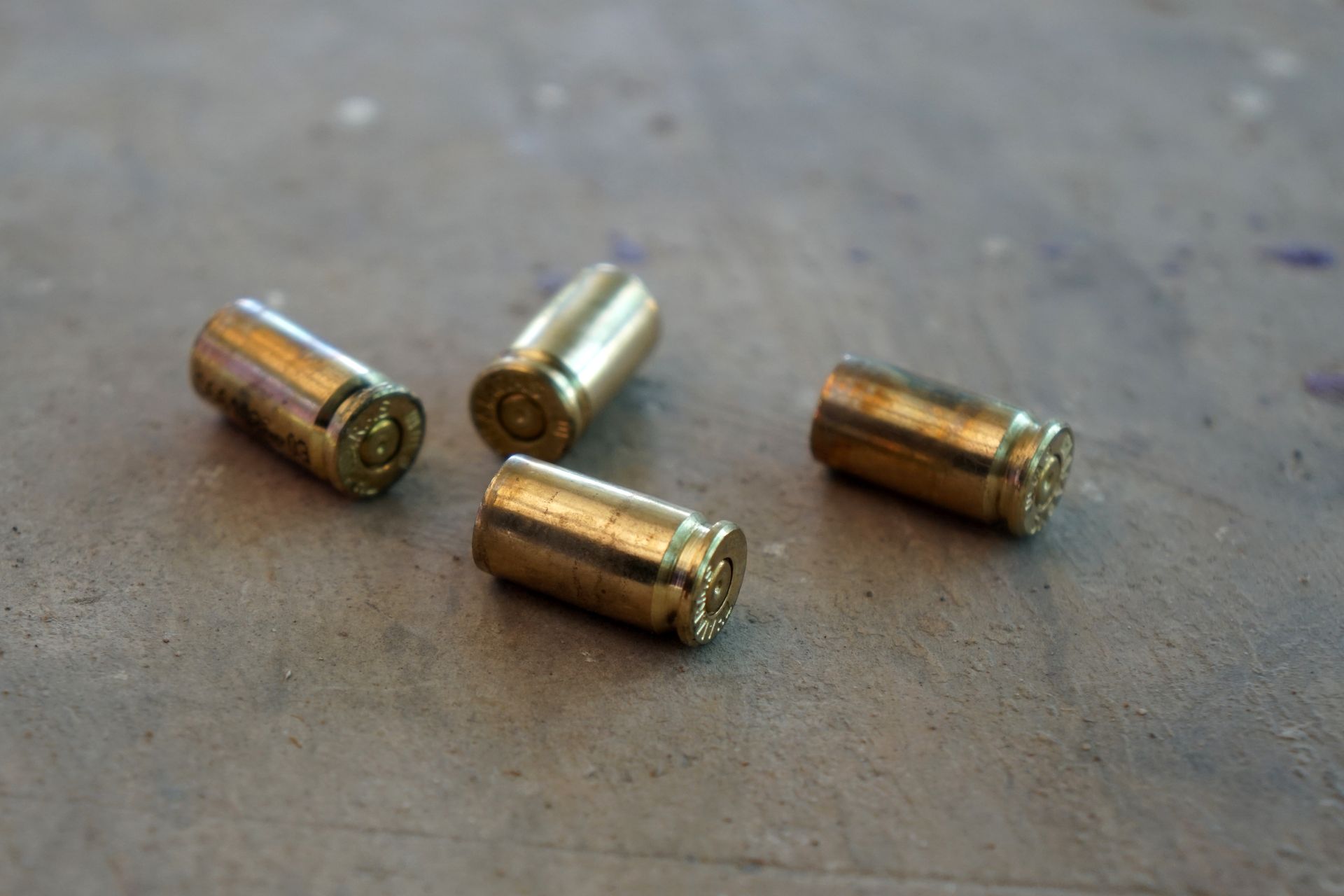 Four brass-colored empty bullet casings scattered on a rough, gray concrete surface.