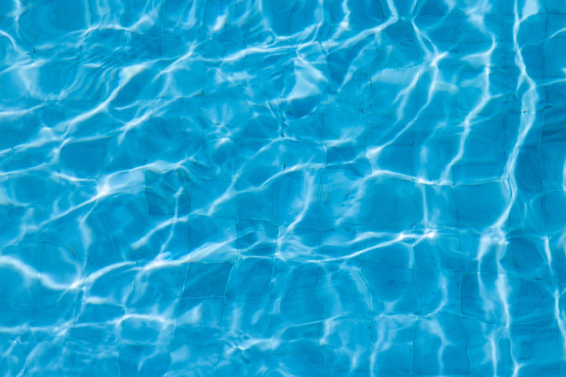 A close-up view of rippling, vibrant blue water with bright, shimmering light reflections on the surface.