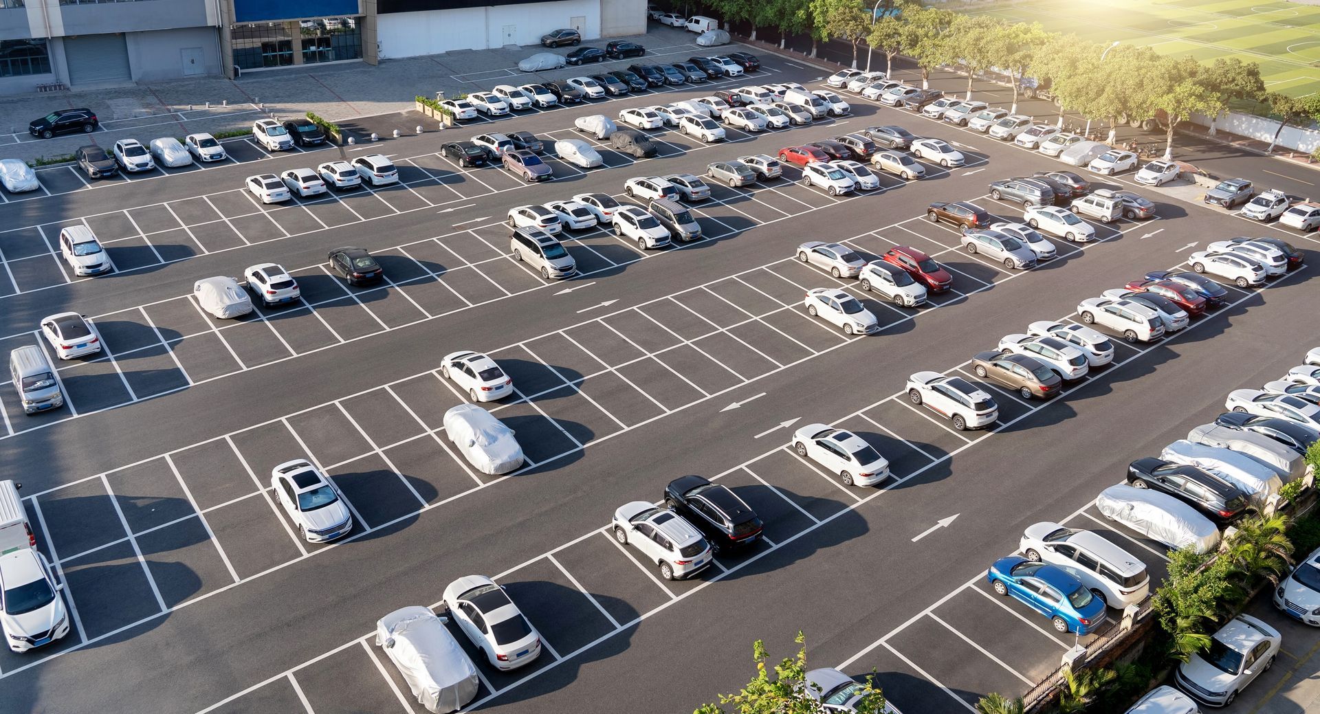 An aerial view of a large, paved parking lot filled with many cars parked in orderly rows on a sunny day.