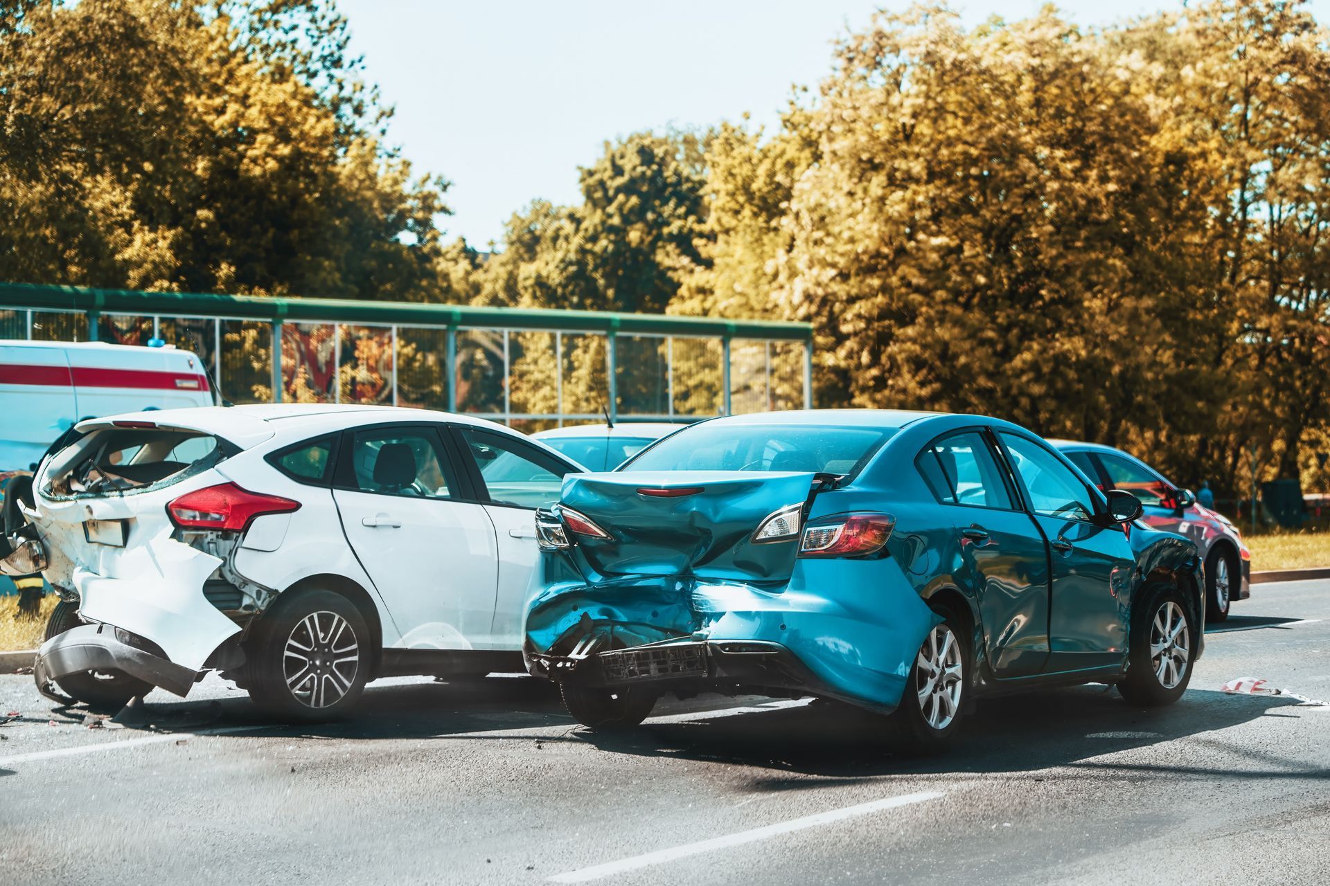 A white hatchback and a teal sedan are damaged on a road after a rear-end collision.