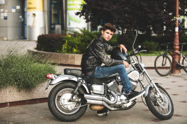 A young man in a leather jacket is sitting on a motorcycle.