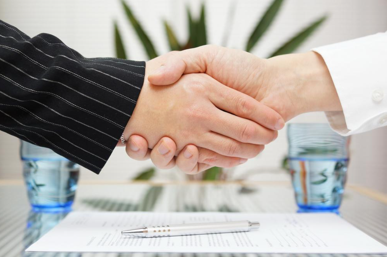 Two people shaking hands over a piece of paper