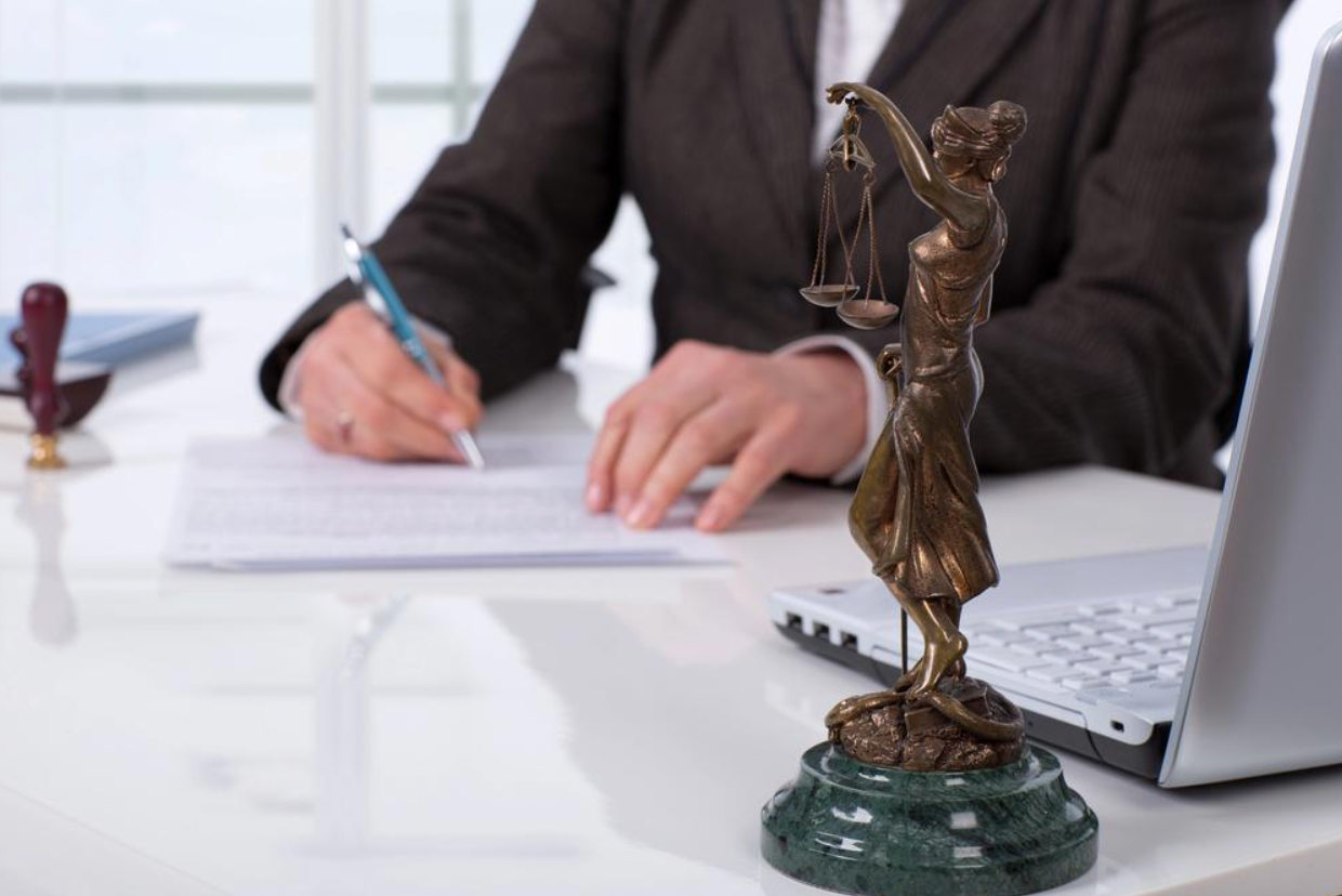 A woman is sitting at a desk with a statue of lady justice and a laptop.