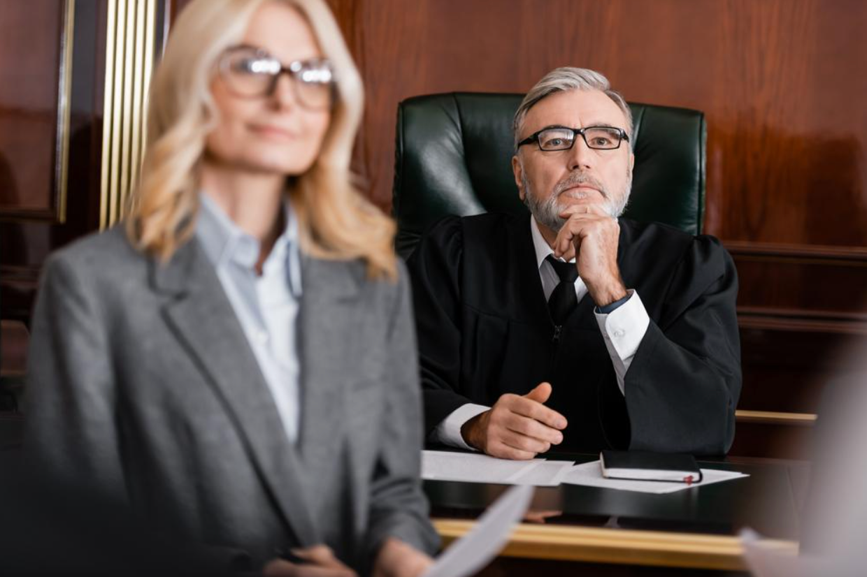 A judge and a lawyer are sitting at a table in a courtroom.